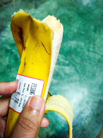 Eine Hand hält eine halb geschälte Banane mit einem Preisschild, das das Gewicht und den Preis angibt.