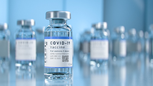 COVID-19-Impfstofffläschchen auf einem Tisch, mit einer klaren Flüssigkeit und einem Etikett, das wichtige Informationen enthält.