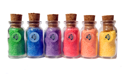 Sechs kleine Glasfläschchen mit Korken, gefüllt mit buntem Sand in den Farben Grün, Blau, Lila, Pink, Orange und Gelb.