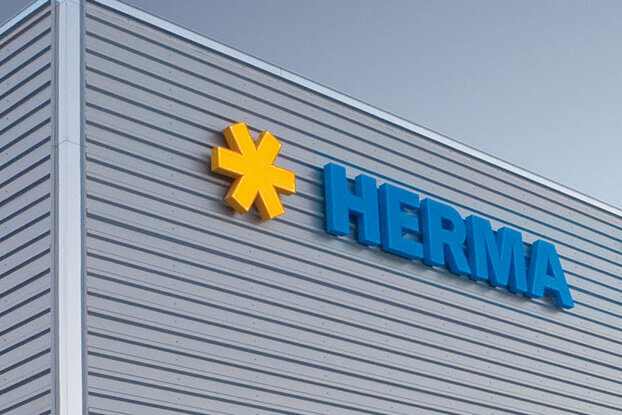 Fassade eines modernen Gebäudes mit dem Logo "HERMA" in blauer Schrift und einem gelben Symbol.
