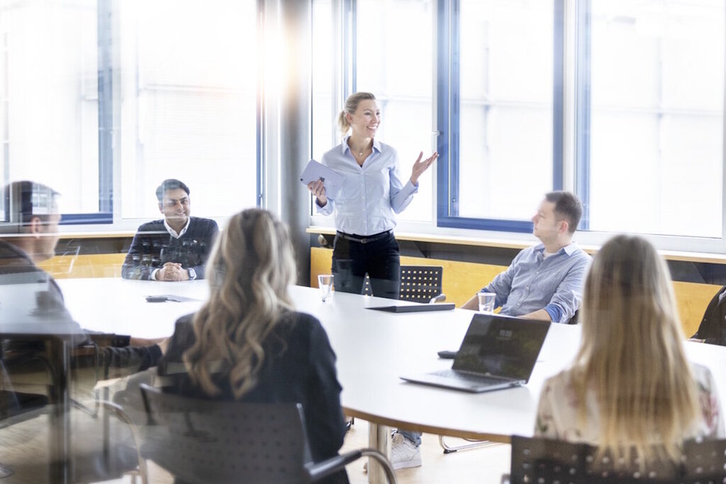 Gruppendiskussionen in einem modernen Büro, mit Personen, die in einem Besprechungsraum sitzen und einem Redner, der präsentiert. 