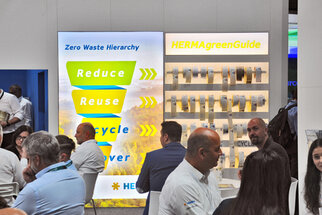Wand mit Informationen zur Zero Waste Hierarchie, die die Begriffe Reduzieren, Wiederverwenden, Recyceln und Entsorgen zeigt. Daneben eine Präsentation von HERMAgreenGuide.