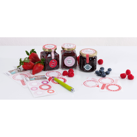 Drei Gläser Marmelade mit bunten Etiketten, umgeben von frischen Erdbeeren, Himbeeren und Blaubeeren sowie Aufklebern und einem grünen Stift.