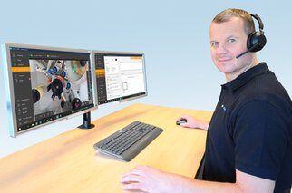 Ein Mann sitzt an einem Schreibtisch mit zwei Monitoren, die technische Software und eine Kameraansicht zeigen. Er trägt ein Headset.