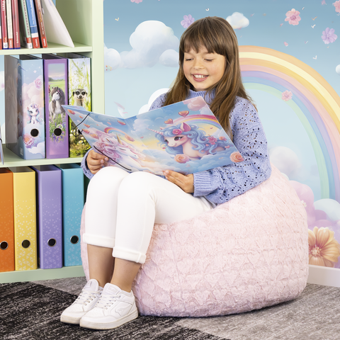 Ein Mädchen sitzt auf einem Sitzsack und liest ein Buch mit einem Einhorn-Cover. Im Hintergrund sind bunte Ordner und eine Regenbogenwand zu sehen.