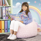Ein Mädchen sitzt auf einem Sitzsack und liest ein Buch mit einem Einhorn-Cover. Im Hintergrund sind bunte Ordner und eine Regenbogenwand zu sehen.