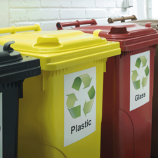 Drei Abfallbehälter in verschiedenen Farben: Gelb für Plastik, Rot für Glas und Schwarz für Restmüll, mit Recycling-Symbolen.
