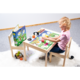 Ein Mädchen sitzt an einem Tisch und spielt mit bunten Spielzeugen und einem Puzzle, umgeben von einer fröhlichen, blühenden Landschaft.