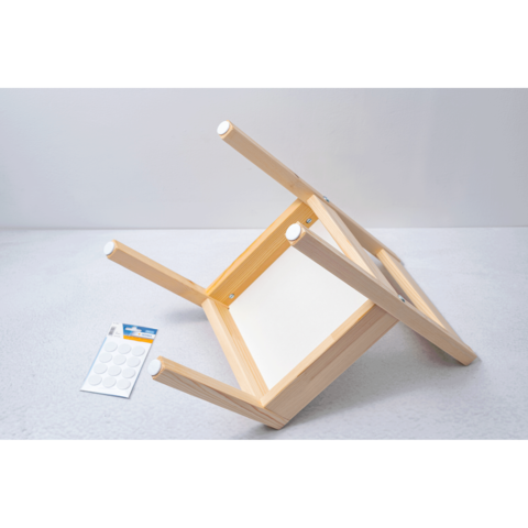 Umgedrehter Holzstuhl mit sichtbarem Sitz und einer Packung selbstklebender Polster auf einer grauen Oberfläche.