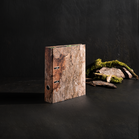 Ein Ordner mit einer Holzmaserung, der auf einer dunklen Oberfläche steht, neben einigen Steinen und Moos.