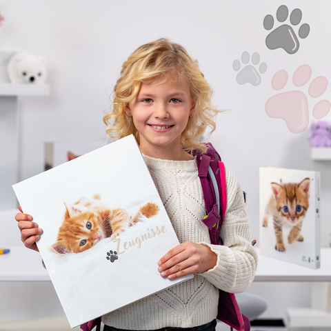 Ein Mädchen mit blonden Locken hält einen Ordner mit einem Katzenbild. Im Hintergrund sind weitere Ordner und Spielzeug zu sehen.