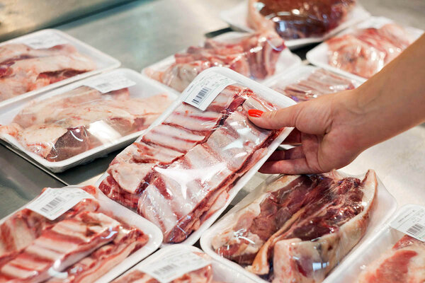 Lebensmittelkennzeichnung: Produktkennzeichnungsetikett, Lebensmitteletikett auf Fleischverpackung, Frau entnimmt Ware aus Kühltheke