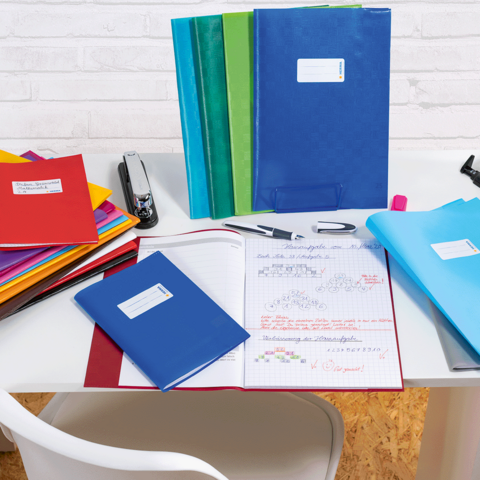 Eine Frau und ein kleines Mädchen sitzen an einem Tisch und blättern durch ein Heft. Bunte Stifte und ein Block liegen auf dem Tisch.