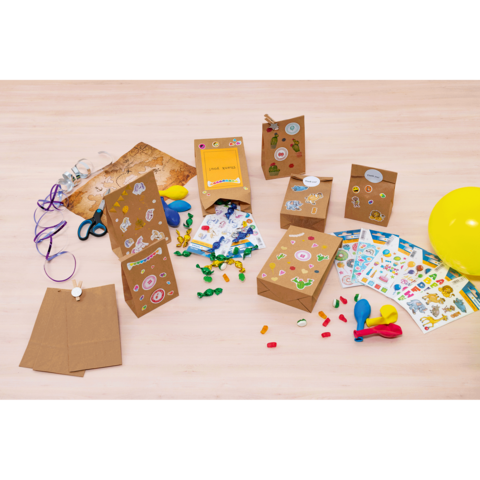 Bastelmaterialien auf einem Tisch, darunter dekorierte Papiertüten, Aufkleber, Ballons, Scheren und bunte Süßigkeiten.