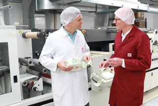 Zwei Personen in Schutzkleidung stehen in einer Produktionsumgebung und diskutieren über umweltfreundliche Verpackungsbanderolen.