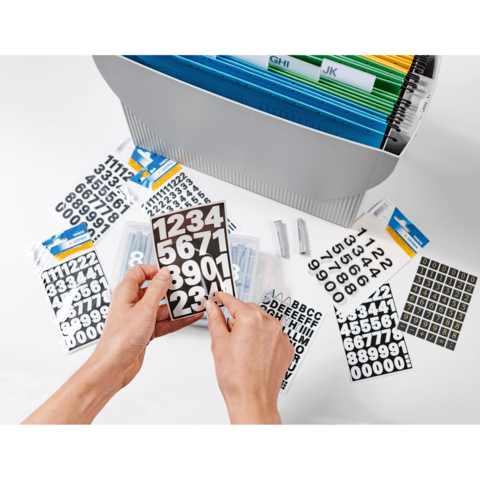 Hände halten ein Blatt mit Zahlenstickern, umgeben von weiteren Stickern und einem Ordner mit farbigen Trennblättern.