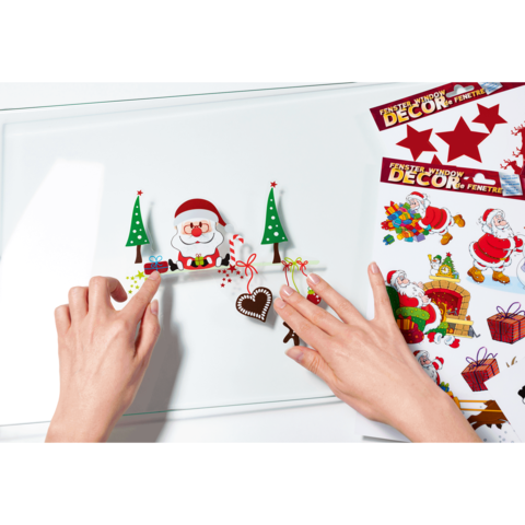 Hände arrangieren Weihnachtsdekorationen, darunter ein Weihnachtsmann, Tannenbäume und ein Herz. Umgeben von Aufklebern und Geschenken.