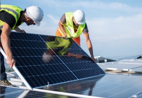 Zwei Arbeiter installieren Solarpanels auf einem Dach, tragen Sicherheitswesten und Helme, während sie ein Panel anheben.