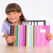 Ein Mädchen hält eine Reihe von bunten Heften in verschiedenen Farben und lächelt dabei.