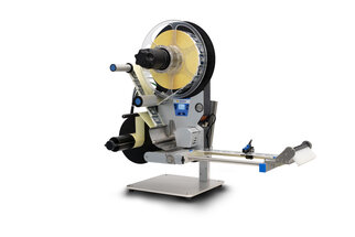 Eine Etikettiermaschine mit einer Rolle Etiketten, einem Abroller und einem Ausgabemechanismus auf einem stabilen Standfuß.