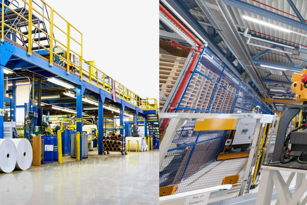 Fabrikhalle mit blauen Maschinen, großen Rollen Papier und einem Roboterarm, der eine Rolle aufnimmt.