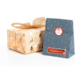 Geschenkpaket mit goldener Schleife und weihnachtlichem Papier, neben einer blauen Tüte mit dem Aufdruck "Frohe Weihnachten".