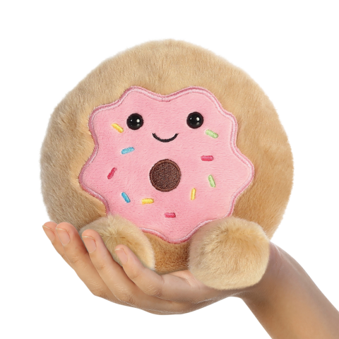 Ein handgehaltener, runder Plüschkeks mit einer rosa Glasur und bunten Streuseln, der ein lächelndes Gesicht hat.