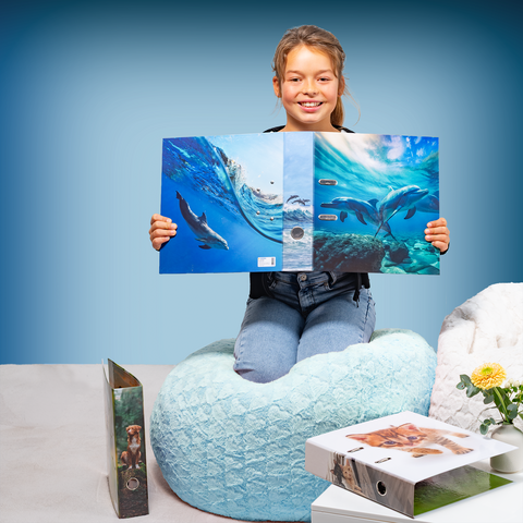 Ein Mädchen sitzt auf einem Sitzsack und hält ein Buch mit Bildern von Delfinen. Neben ihr liegen weitere Bücher auf einem Tisch.