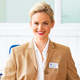 Eine lächelnde Frau mit blonden Haaren trägt einen beigen Blazer und eine weiße Bluse. Ein Namensschild mit "Manuela Richter" ist sichtbar.
