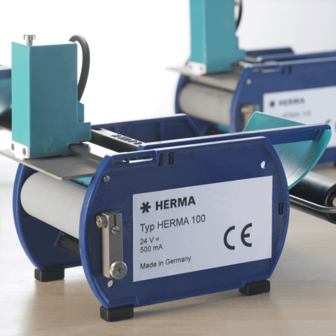 Typ HERMA 100 Etikettiermaschine, 24 V, 500 mA, hergestellt in Deutschland, mit blauer und grauer Gehäusefarbe.