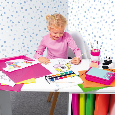 Ein kleines Mädchen sitzt an einem Tisch, malt mit Wasserfarben und umgeben von buntem Papier und Zeichnungen.