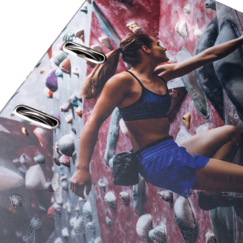 Eine Kletterin in Sportbekleidung erklimmt eine Kletterwand mit bunten Griffen. Sie konzentriert sich auf ihren nächsten Halt.