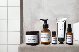 Eine Auswahl an Naturkosmetikprodukten, darunter Gesichtscreme, Reinigungsgel, Zahnöl, Handcreme und Serum, auf einer grauen Oberfläche.