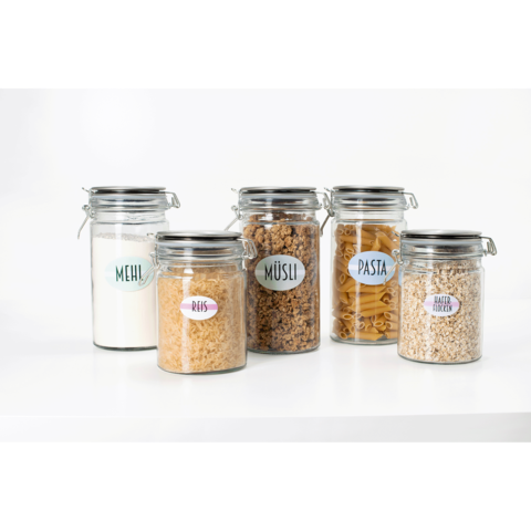 Fünf Glasbehälter mit Deckel, gefüllt mit Mehl, Reis, Müsli, Pasta und Haferflocken, jeweils mit beschrifteten Etiketten.