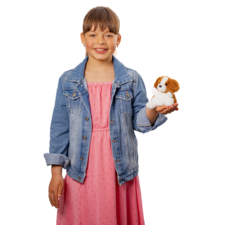 Ein Mädchen in einem rosa Kleid und einer Jeansjacke hält ein Stofftier in Form eines Hundes in der Hand und lächelt.