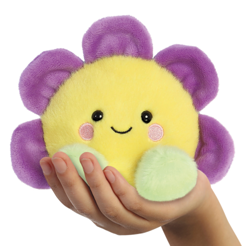 Eine Hand hält ein gelbes, lächelndes Plüschspielzeug in Blumenform mit lila Blütenblättern und grünen Blättern.