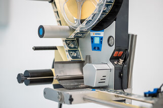 Etikettiermaschine mit Rollen, Steuerungselementen und einem Display, bereit zum Etikettieren von Produkten.