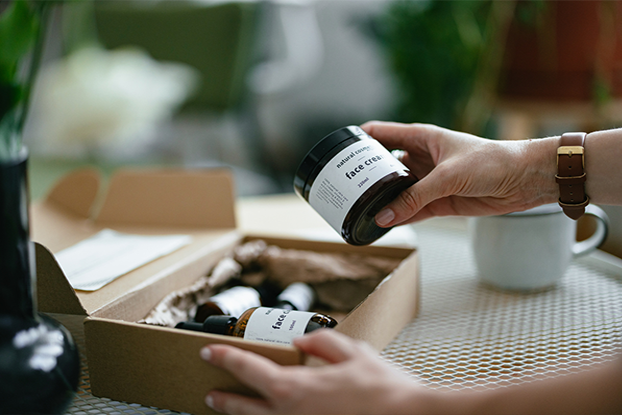 Ein beschlagener Fenster mit einem Folienetikett als Warnschild, eine Person öffnet eine Box mit beschrifteten Behältern, und eine andere Person versucht ein Folienaufkleber zu zerreißen.