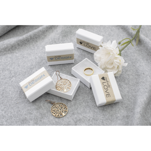 Schmuckstücke in weißen Geschenkboxen, darunter Ohrringe und ein Ring, auf einem grauen Untergrund mit einer Blume.