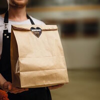 Ein Mann in einem schwarzen Schürze hält eine braune Papiertüte mit einem Aufkleber "Homemade Spices".
