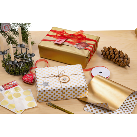 Geschenkverpackungen in Gold und Weiß mit Punkten, umgeben von Dekorationen wie Kerzen, Tannenzapfen und Geschenkband auf einem Tisch.