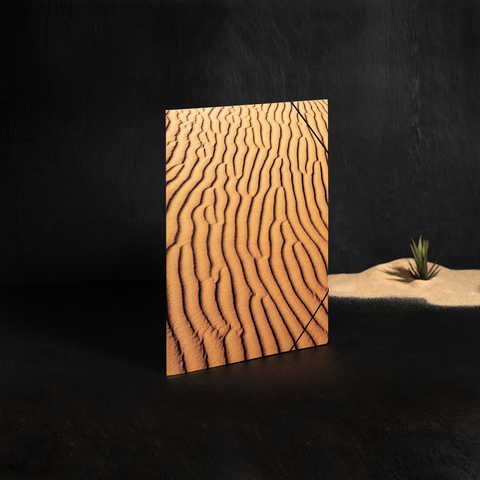 Ein Notizbuch mit einem Cover, das Wellenmuster in sandfarbener Textur zeigt, steht auf einem dunklen Untergrund.
