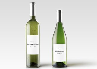 Zwei Flaschen Weißwein mit Etiketten: eine Chardonnay aus 2016 und eine Riesling aus 2017, beide mit dem Namen "HERMAexquisite".