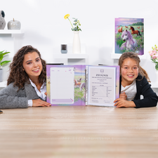 Zwei Mädchen sitzen an einem Tisch und halten ein offenes Heft mit einem Zertifikat und einem leeren Blatt. Im Hintergrund sind dekorative Elemente sichtbar.