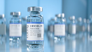 COVID-19-Impfstofffläschchen auf einem Tisch, mit einer klaren Flüssigkeit und einem Etikett, das wichtige Informationen enthält.