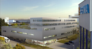 Moderne Bürogebäude mit großen Fenstern und begrünten Dächern, beschriftet mit "HERMA". Lkw und Autos parken in der Nähe.