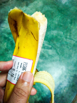 Eine Hand hält eine halb geschälte Banane mit einem Preisschild, das das Gewicht und den Preis angibt.
