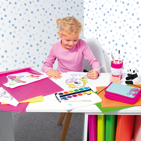 Ein kleines Mädchen sitzt an einem Tisch und malt mit Wasserfarben. Um sie herum liegen bunte Blätter und Zeichnungen.