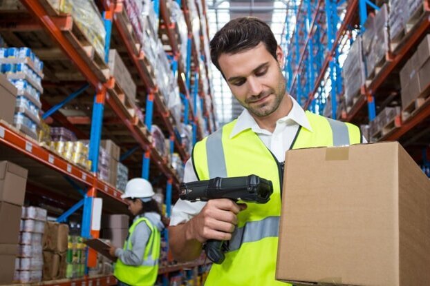 Logistikmitarbeiter beim Einscannen eines Versandetiketts auf einem Karton, im Lager, Querformat