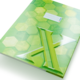 Grünes Notizbuch mit hexagonalem Muster und einem großen, glänzenden Logo in der Mitte. Ein Etikett für Beschriftungen ist sichtbar.